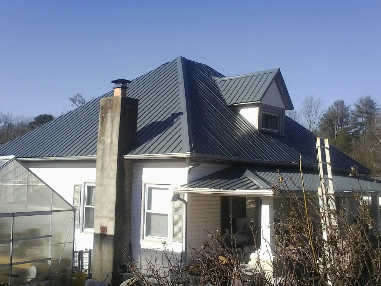 Dark blue standing seam metal roof on a white farmhouse with dormer — Slate & Tile Roof Repair by Roofing Brothers in Pierce
