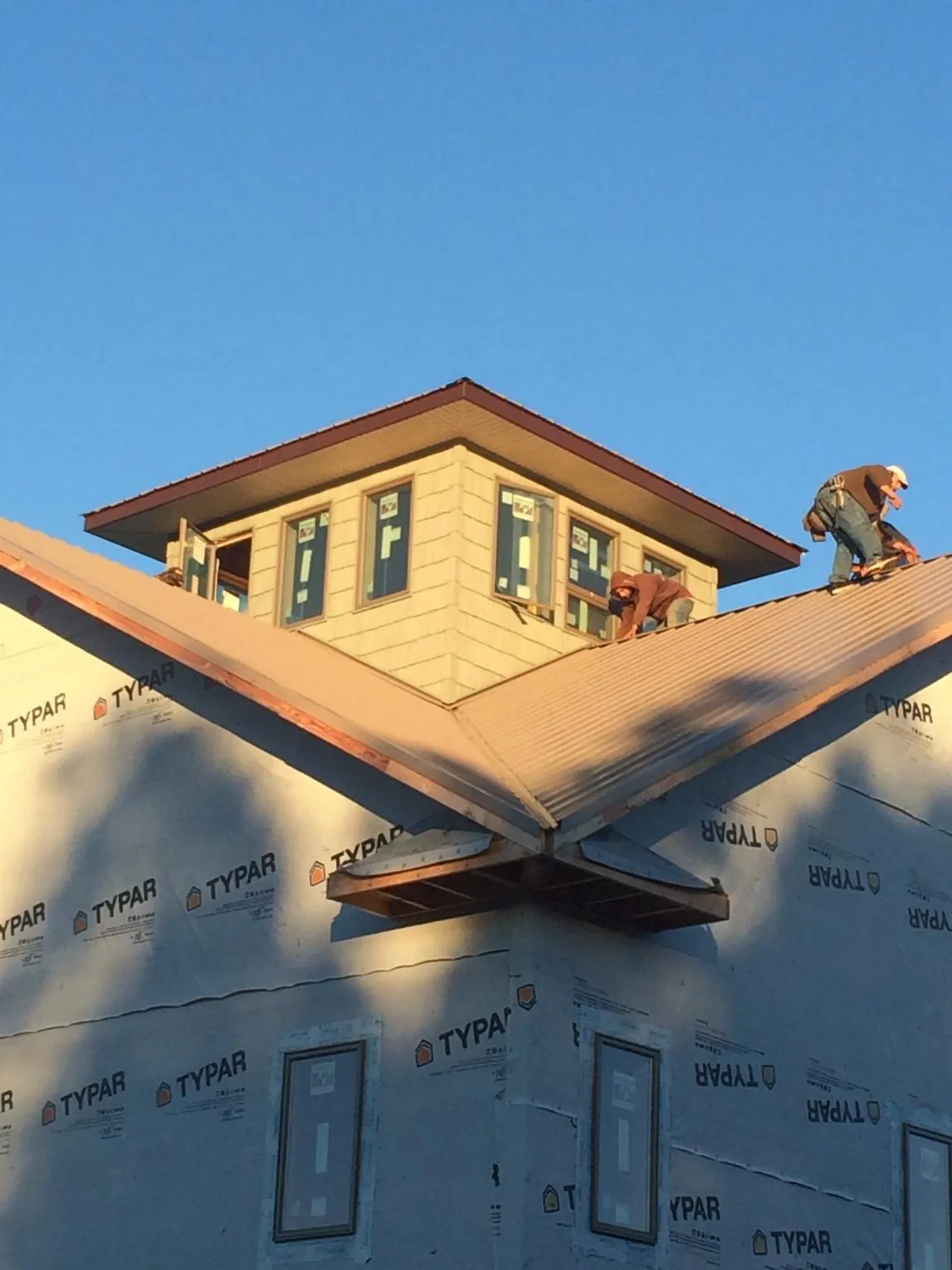 Roofers working around a rooftop cupola on a new metal roof at sunset — Roof Waterproofing in Pierce by Roofing Brothers